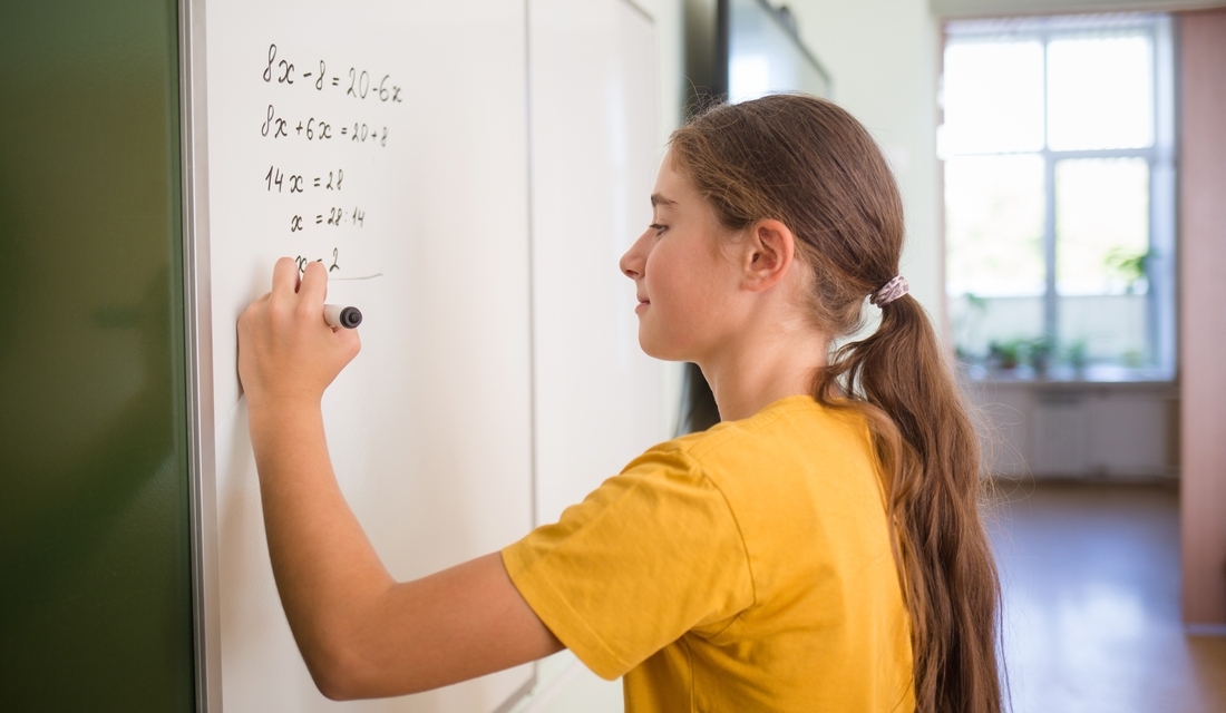 Teenager math student solves the equation on blackboard in school classroom in math algebra lesson