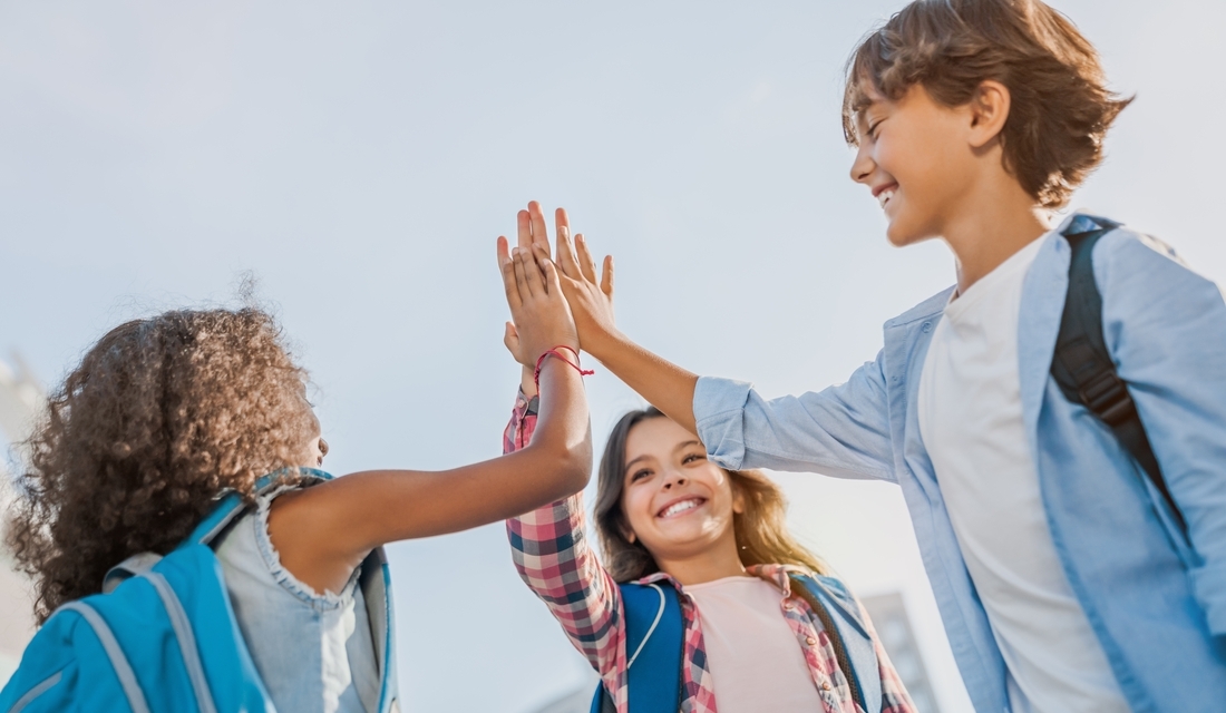 Three middle schoolers with backpacks high-fiving outdoors