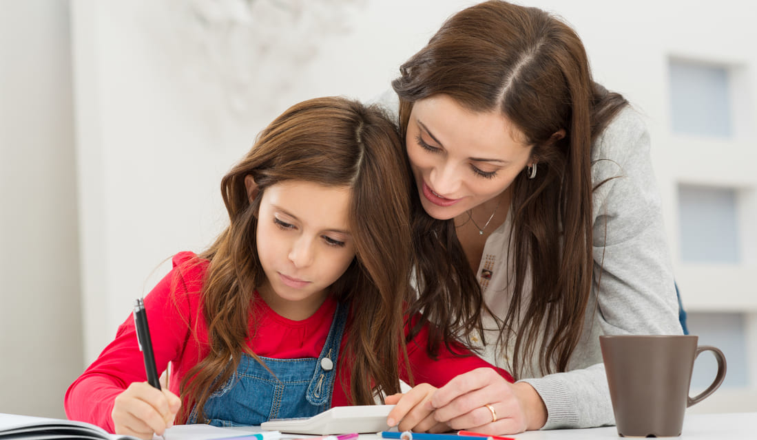 Mother helping her daughter with math homework at the kitchen table, both focused and engaged in the activity