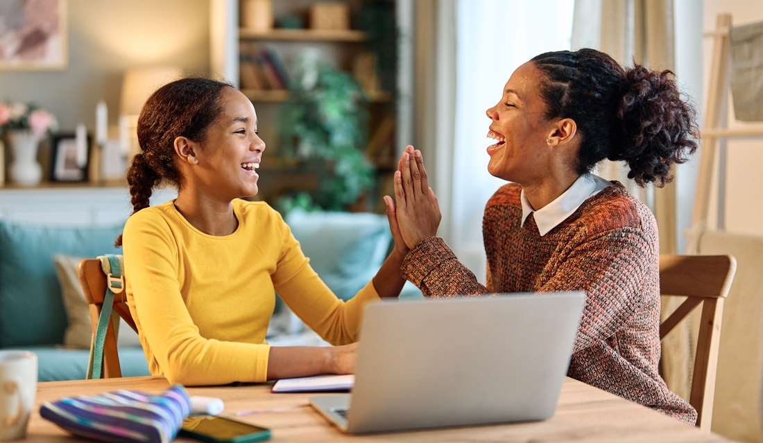 Mother and daughter smiling and giving a high five at a table while working on schoolwork together at home