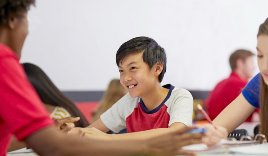 A group of students engaged in discussion while sitting around a table in a classroom setting.