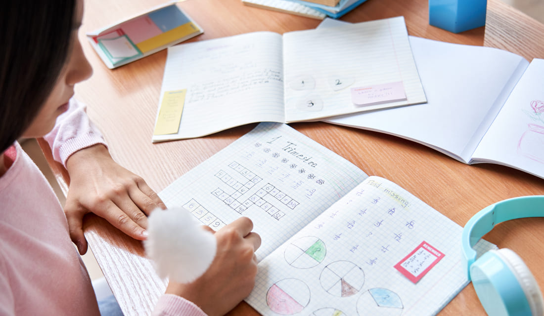 A woman sits at a table, writing in a notebook with a pen, focused on her task.