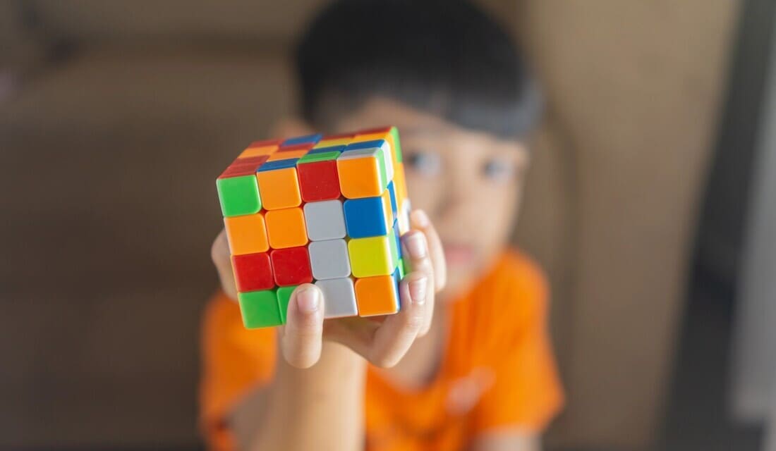 A young boy smiles while holding a colorful Rubik's Cube in his hands, showcasing his interest in puzzles.