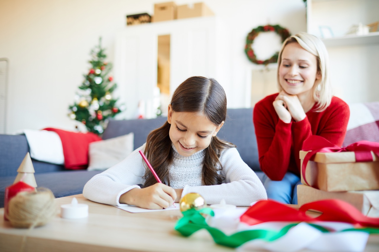 Daughter draws while mother watches and smiles in a Christmas decorated room