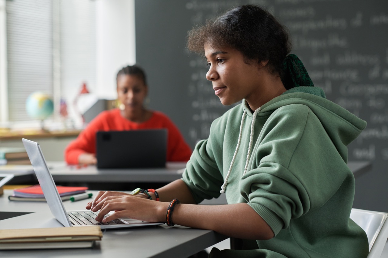 A girl sits at desk working on a laptop