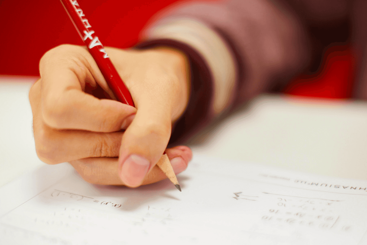 A person writing on paper with a red pencil.
