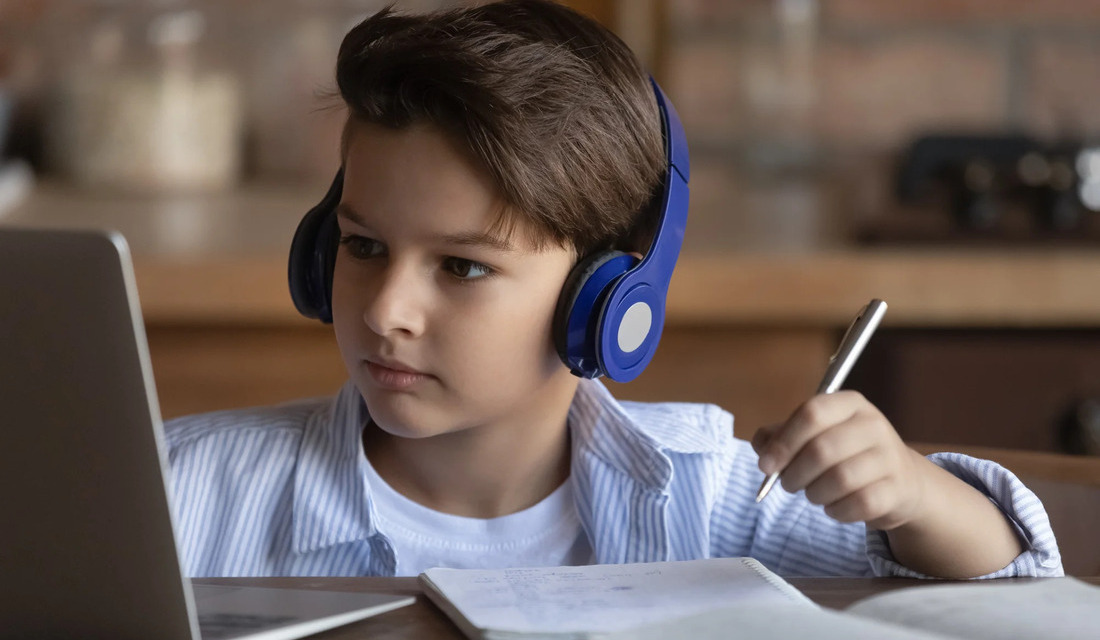A young boy with headphones, intently gazing at a laptop, suggesting he is participating in a digital learning experience.