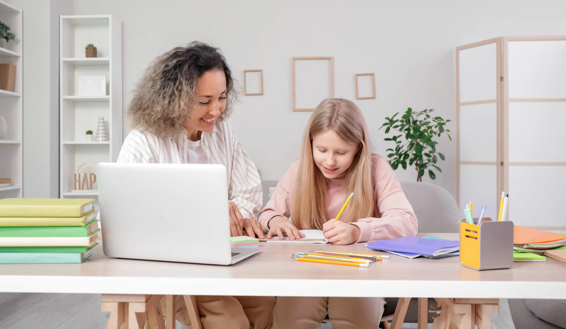 A mother and daughter sit side by side, focused on a laptop, working together on a project or task.