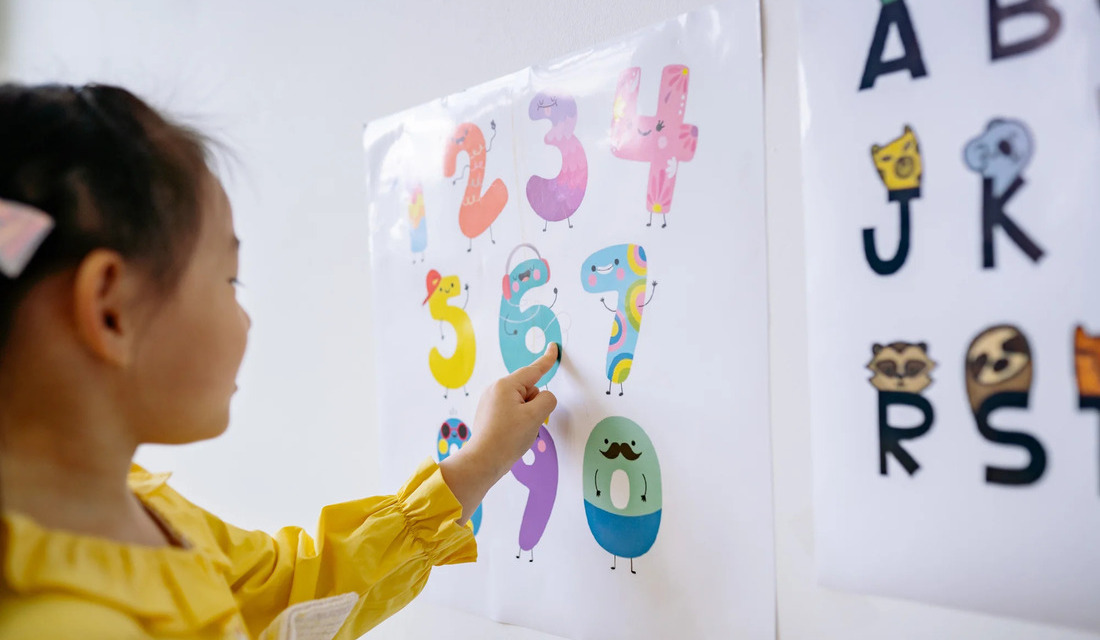 A young girl is pointing at a poster that features a series of numbers, showcasing her curiosity and engagement.