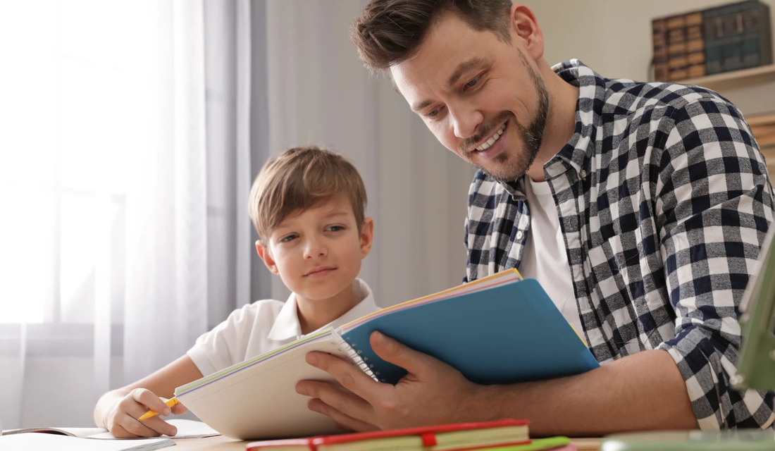 A man and a boy sit at a table, engaged in reading a book together, sharing a moment of learning and connection.