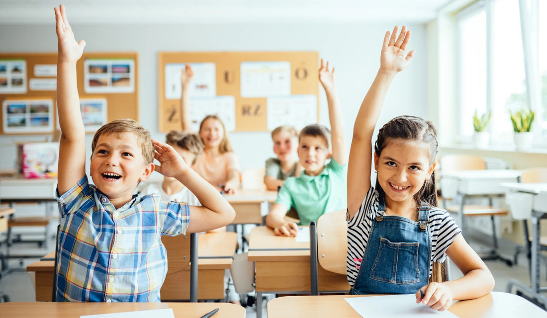 A classroom scene with children eagerly raising their hands to answer questions, showcasing engagement and participation.
