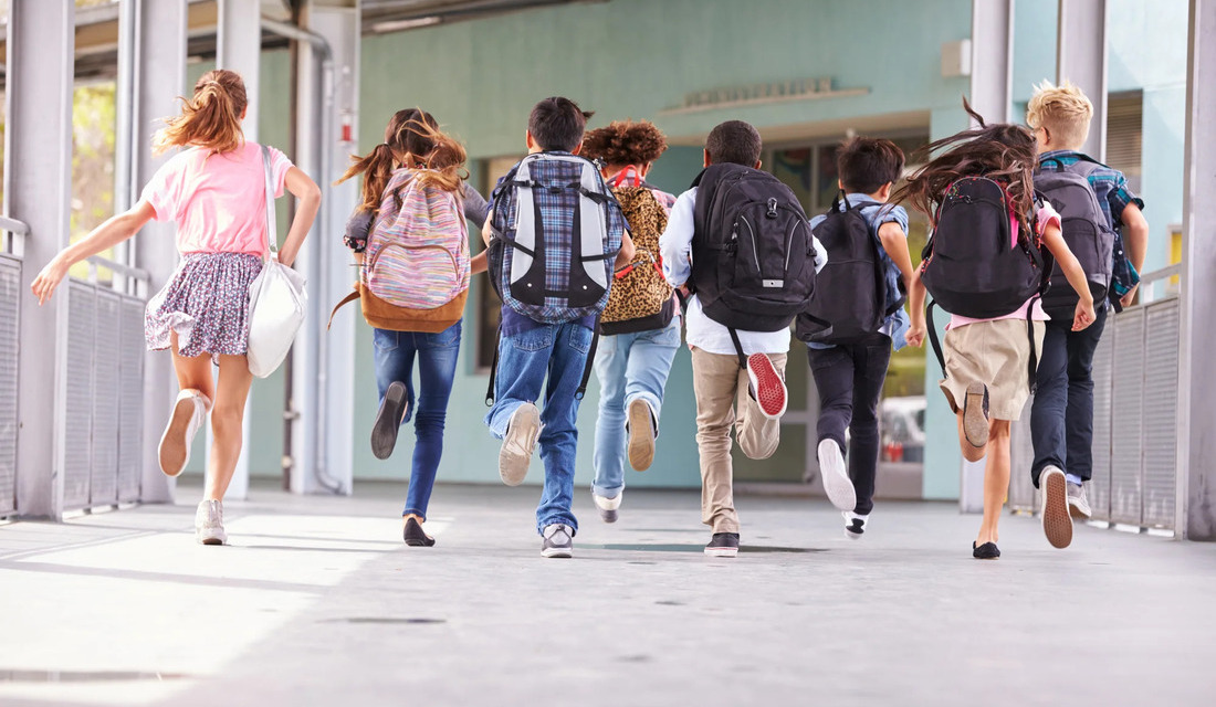 A group of young people joyfully running down a sidewalk on a sunny day.