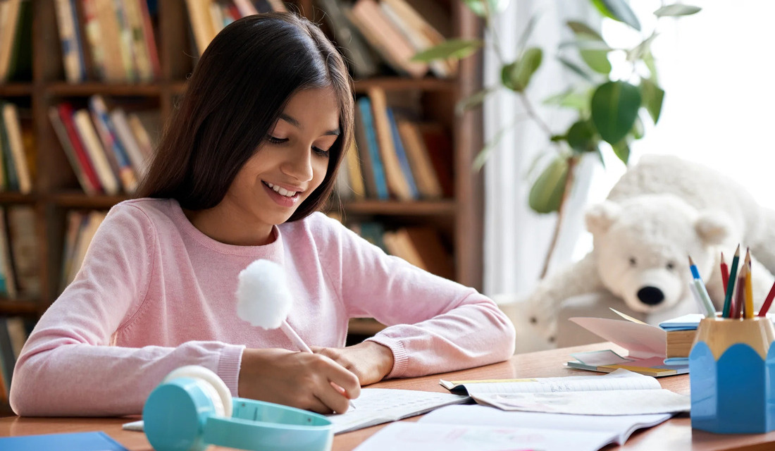 A girl at a desk interacts with a white teddy bear, highlighting a blend of childhood innocence and study time.