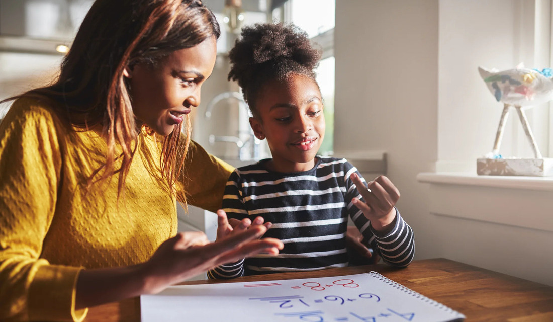 A mother and daughter collaborate on a math problem at a table, focused and engaged in their work.