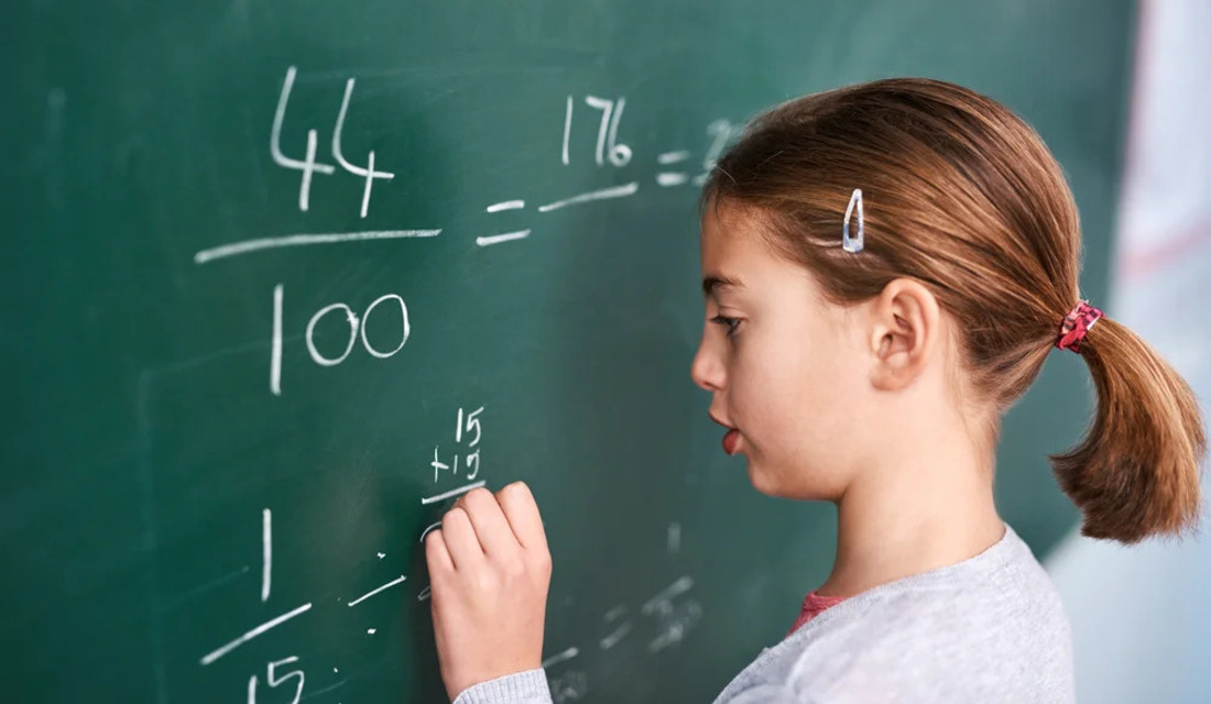 A young girl using chalk to write numbers on a blackboard, demonstrating her learning process.