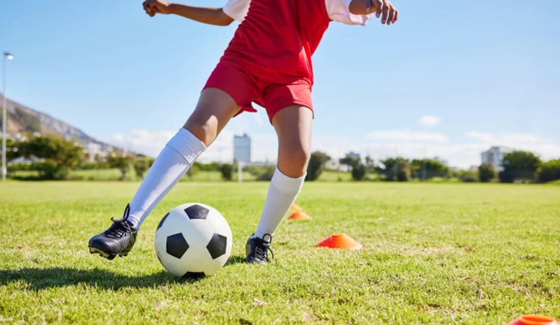 A child energetically kicks a soccer ball on a grassy field, showcasing enthusiasm for the game.