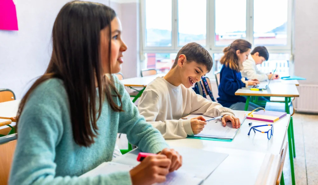 A group of children attentively sitting at desks in a bright classroom, engaged in learning activities.