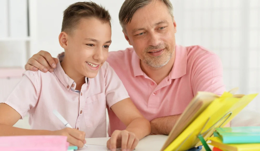 A man and a boy sit at a desk, engaged in reading a book together, sharing knowledge and bonding.