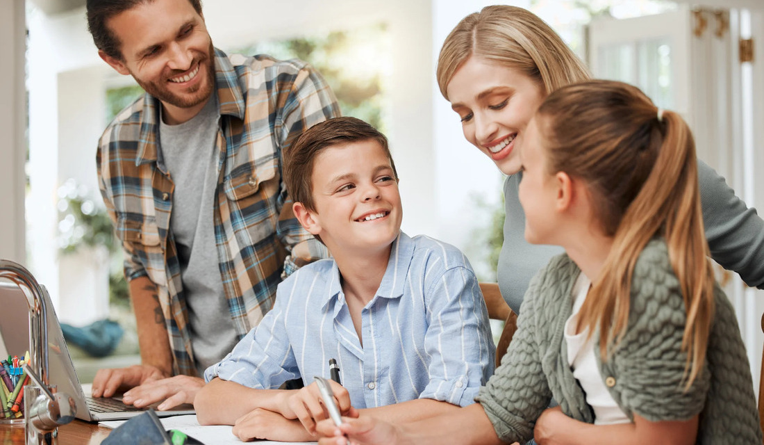 A family of four sits around a table, sharing smiles and conversation.