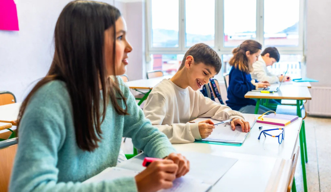 A group of children attentively sitting at desks in a bright classroom, engaged in learning activities.