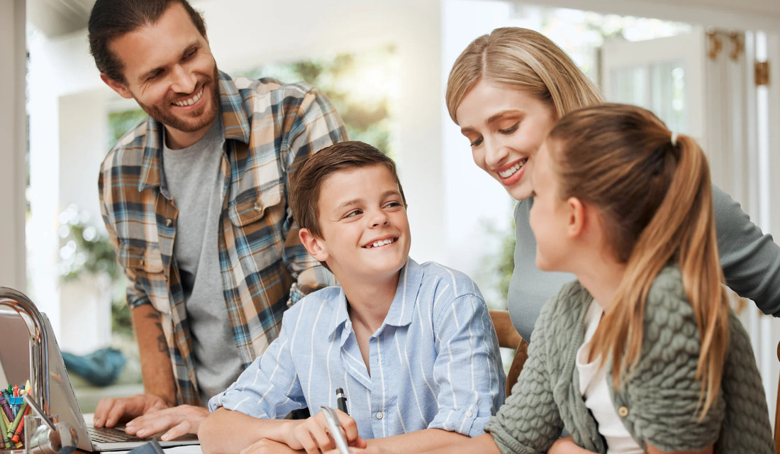 Parents and their two children work together on homework at a table.