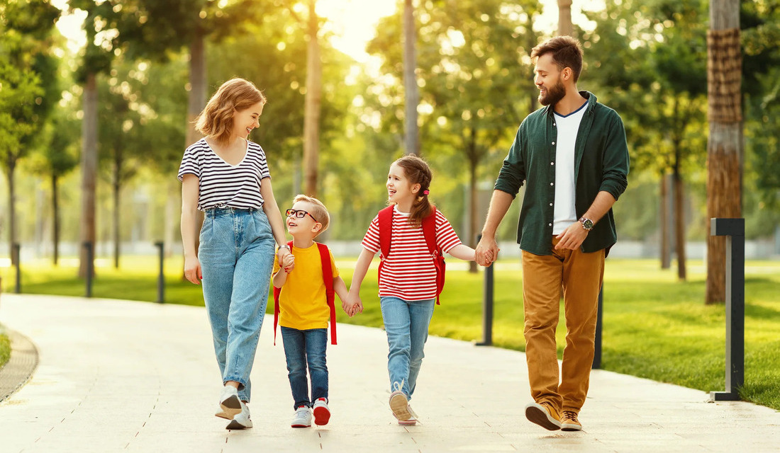 A family of four walking hand in hand through a lush green park, enjoying a sunny day together.