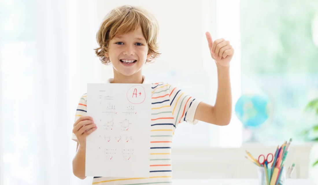 A young boy proudly holds a piece of paper with a pencil, showcasing his artwork or written work.