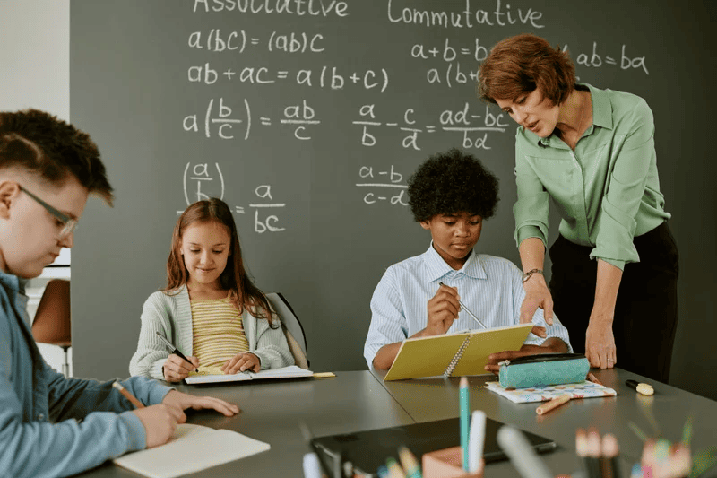 A teacher assists students with math problems, providing guidance and support in a classroom setting.