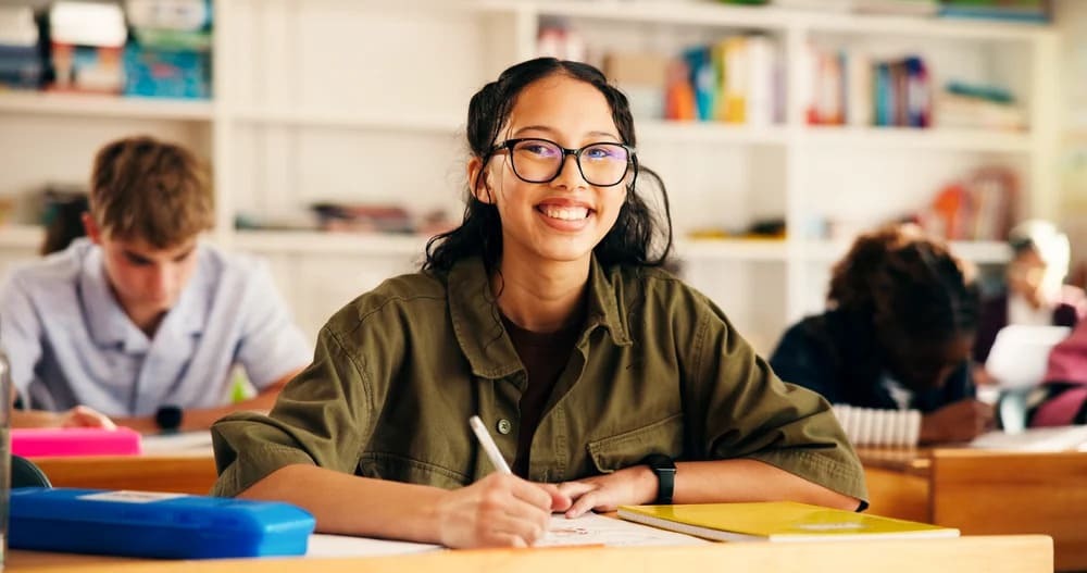 A smiling student in a classroom surrounded by classmates, engaged in a learning environment.