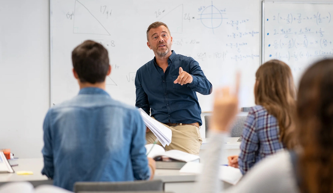 A man presents a lecture to students, who are focused and taking notes in a classroom setting.