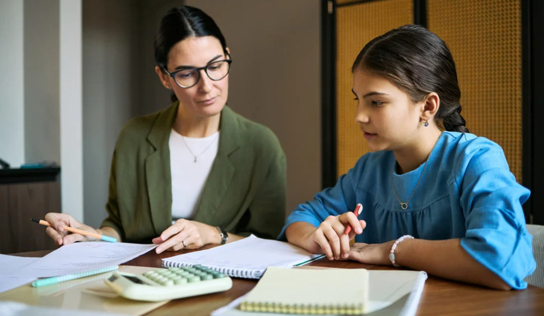 A woman and a girl collaborate on a paper, focused on writing and discussing ideas together at a table.