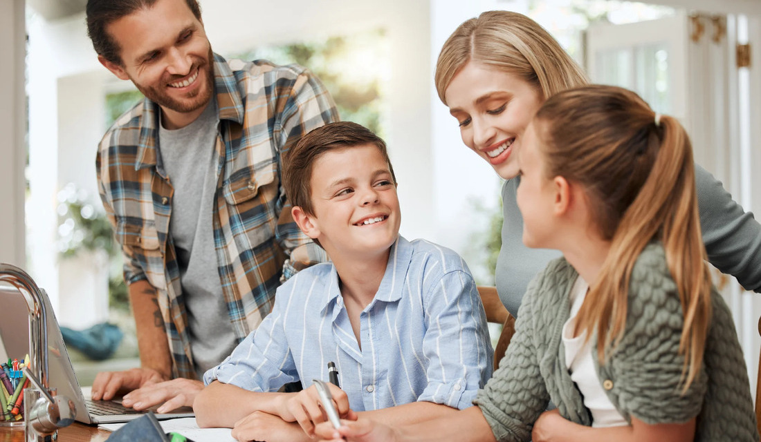 A family gathered around a table, engaging with a laptop while sharing smiles and conversation.