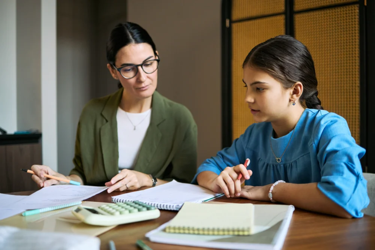 A woman and a girl collaborate on a paper, focused on writing and discussing ideas together at a table.