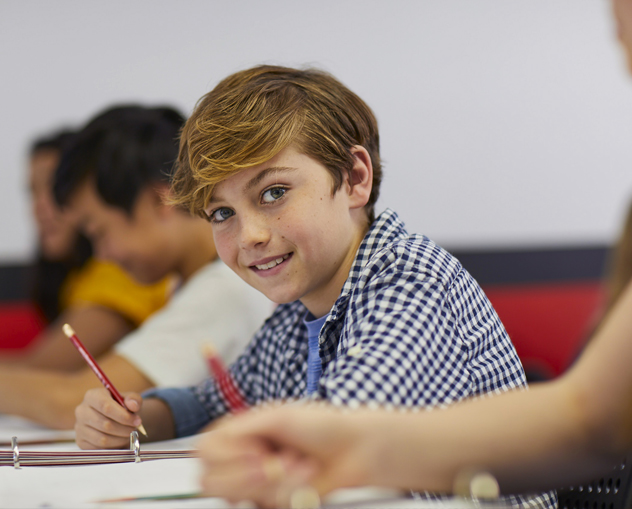 young boy smiling while holding a pen and solving math problems