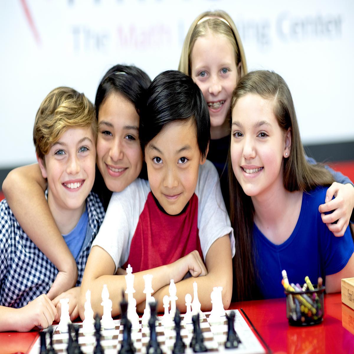 Five students smiling with a chess board on the table in front of them.