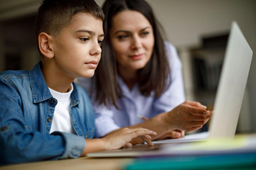 Boy and teacher reviewing math problems on a laptop during a tutoring session.