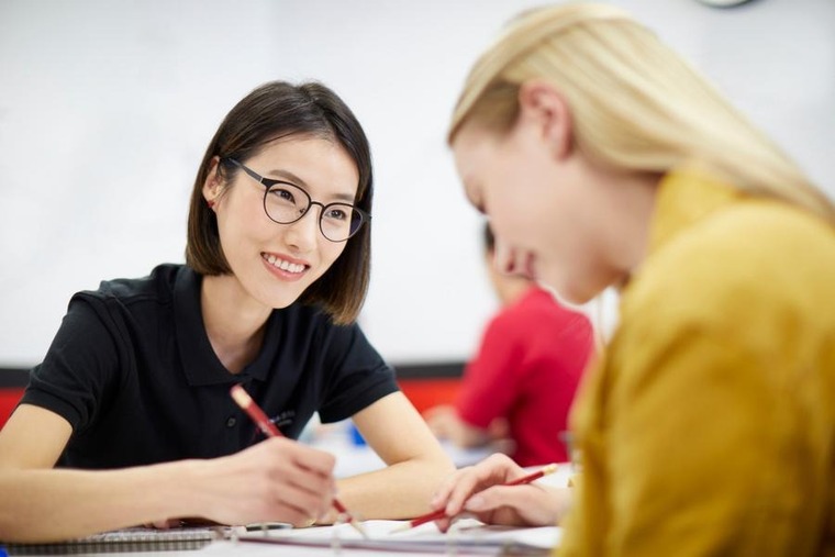 A female student and a female tutor collaborate on writing assignments in a classroom setting.