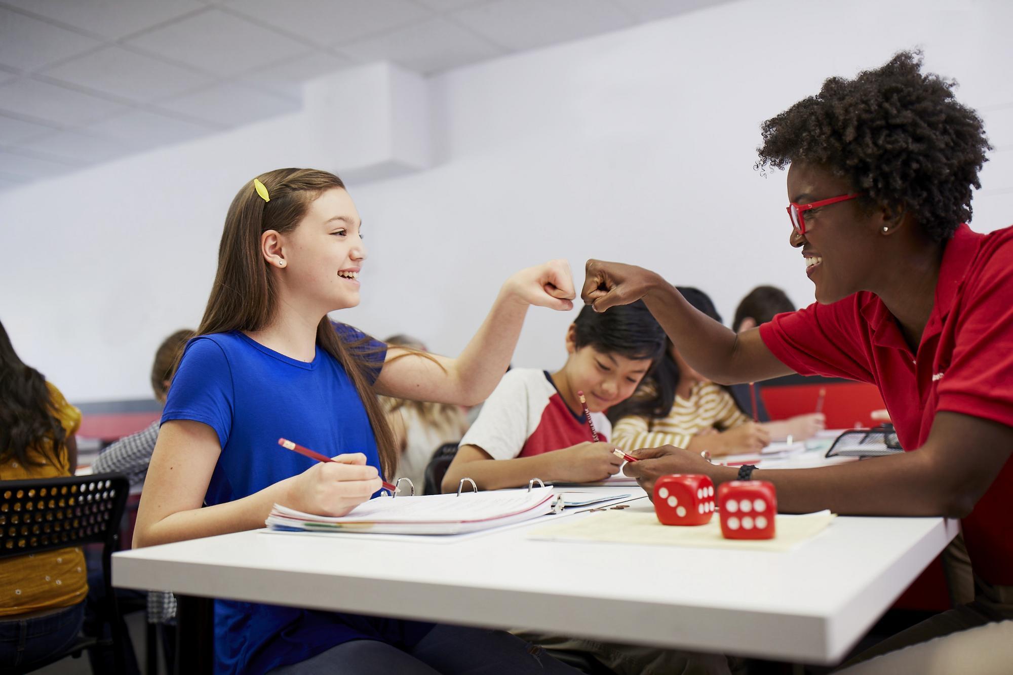 A tutor and students engaged in a dice game in a classroom setting, promoting learning through play.