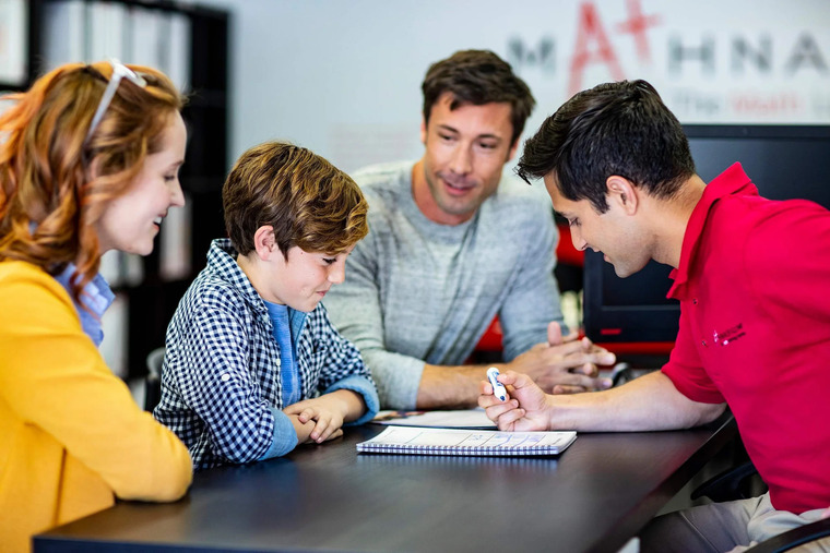 A student and his parents sit at a table with a math tutor in a classroom setting, engaged in learning.