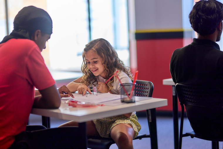 A young girl sits at a table with a man engaged in conversation and sharing smiles.