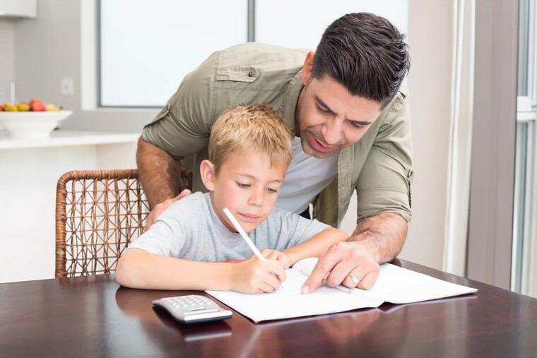 A father and a son collaborate on a project, focused on their work together at a table.