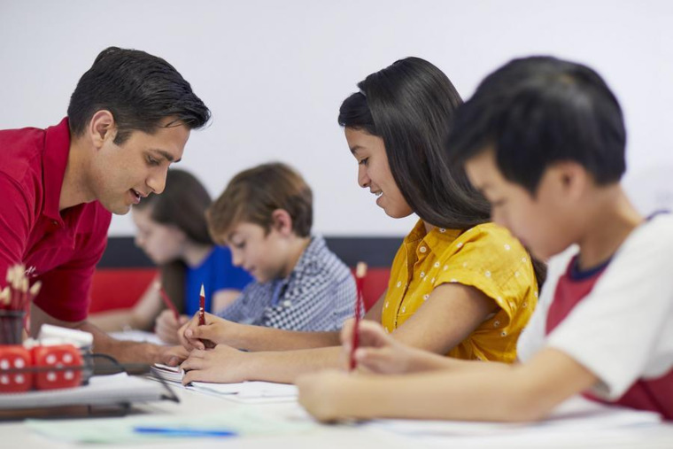 A teacher assists students with their homework, providing guidance and support in a classroom setting.