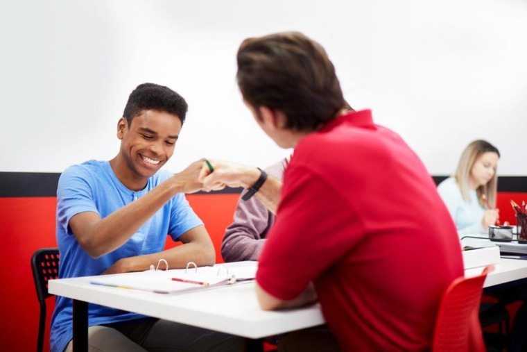 A tutor sits at a table, engaging in conversation with a student, who appears to be listening attentively.