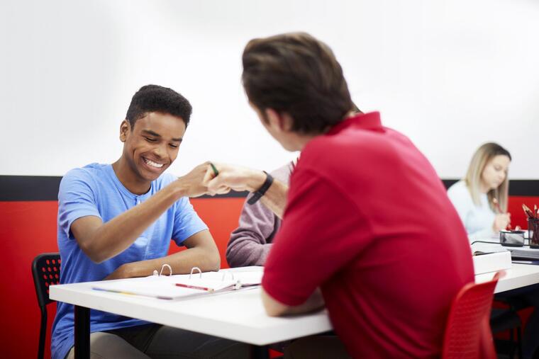 A man and woman sit at a table while one man shakes hands with another man across from them.