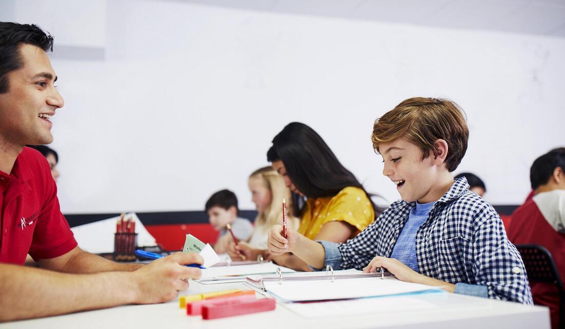 A math tutor interacts with a student at a table, fostering a collaborative learning environment.