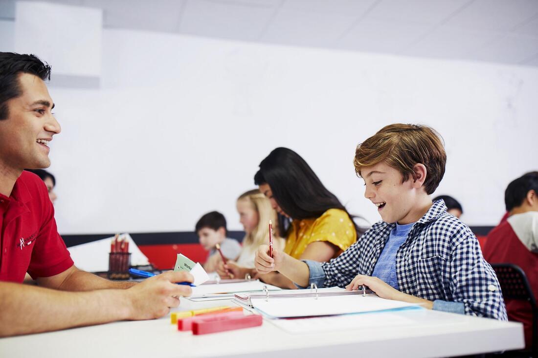 A boy is seated at a table with a teacher, participating in an educational session together.