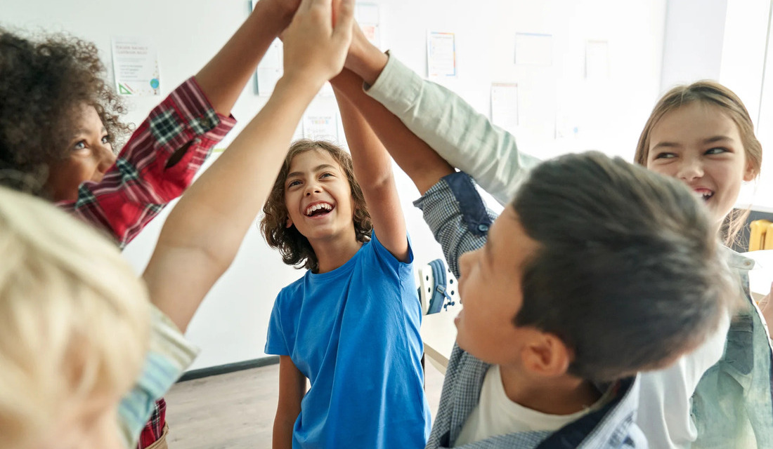 A group of children standing in a circle, holding hands and smiling at each other in a joyful display of friendship.