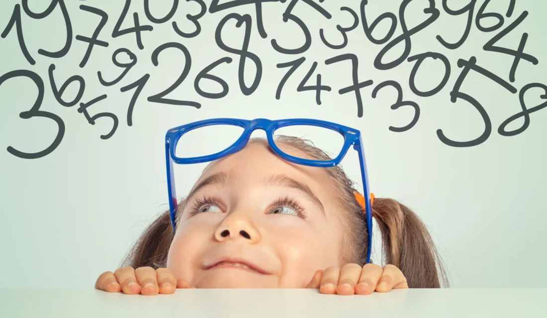 A young girl with glasses gazes upward, observing numbers displayed above her.