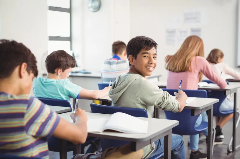 A group of children attentively sitting at desks in a bright classroom, engaged in learning activities.