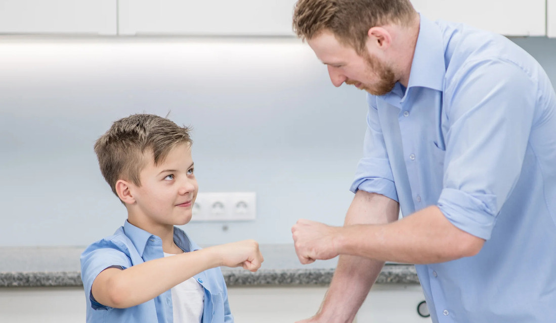 In a kitchen, a man and a boy are playfully fighting with fists, creating a lively and humorous scene.